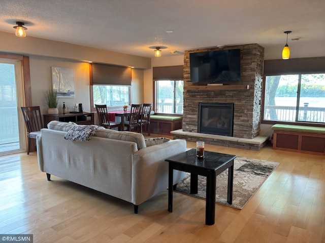 living area with plenty of natural light, light wood-style floors, and a stone fireplace