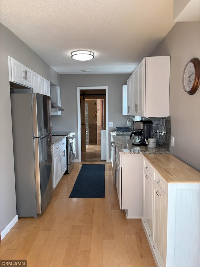 kitchen featuring stainless steel appliances, white cabinets, light wood-style floors, light stone counters, and a sink