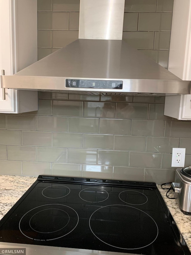 kitchen view of ventilation hood, decorative backsplash, white cabinetry, and black electric stovetop