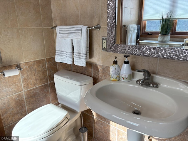 half bath with tile walls, toilet, and a sink