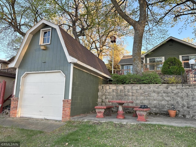 view of property exterior featuring a gambrel roof, concrete block siding, an outbuilding, a garage, and roof with shingles