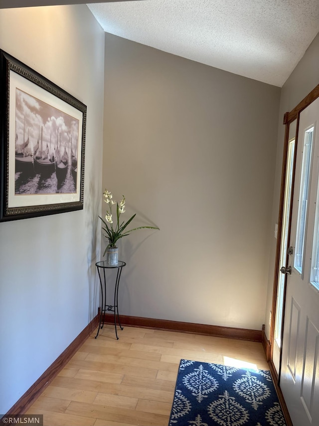 hall featuring light wood-type flooring, baseboards, and a textured ceiling