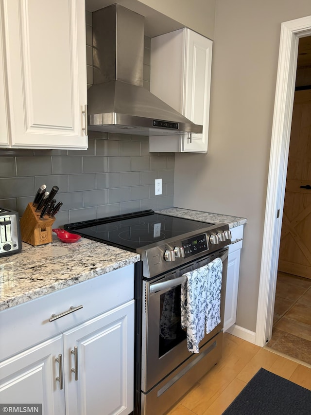 kitchen featuring wall chimney exhaust hood, stainless steel range with electric stovetop, backsplash, and white cabinets