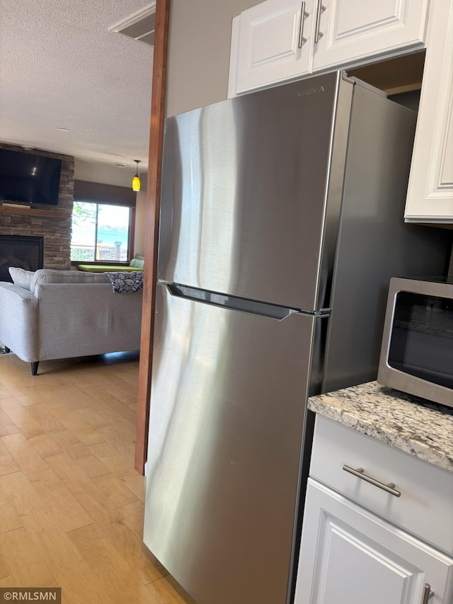 kitchen with appliances with stainless steel finishes, a textured ceiling, white cabinetry, light stone counters, and a fireplace