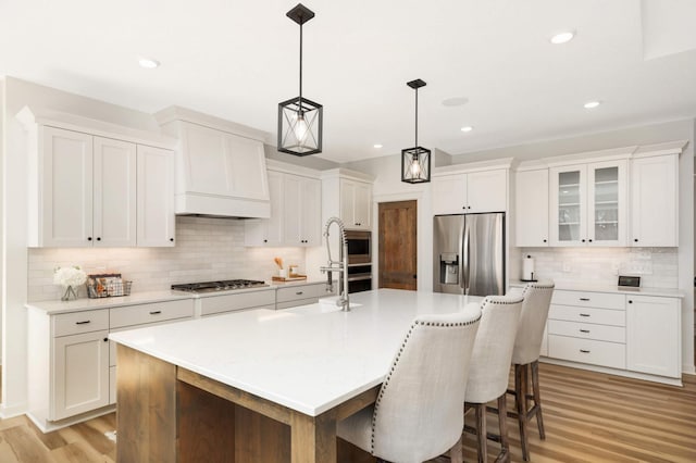15359 Quamba St NE, Ham Lake, MN 55304 - kitchen featuring appliances with stainless steel finishes, decorative backsplash, light wood-type flooring, white cabinets, and a center island with sink
