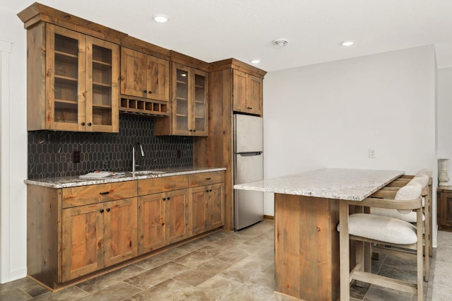15359 Quamba St NE, Ham Lake, MN 55304 - kitchen with freestanding refrigerator, light stone counters, backsplash, a breakfast bar area, and glass insert cabinets