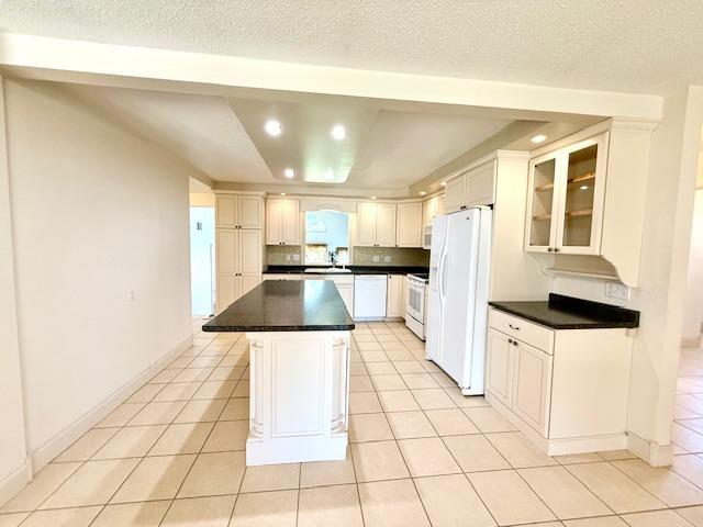 421 Main St E, Eitzen, MN 55931 - kitchen featuring white appliances, dark countertops, light tile patterned floors, a center island, and glass insert cabinets