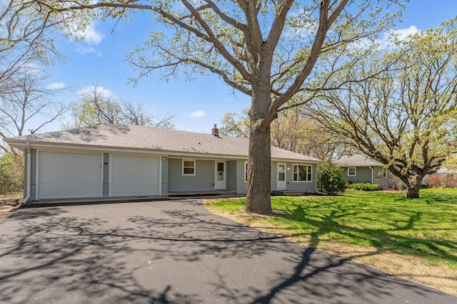 single story home featuring asphalt driveway, an attached garage, a front yard, and a chimney