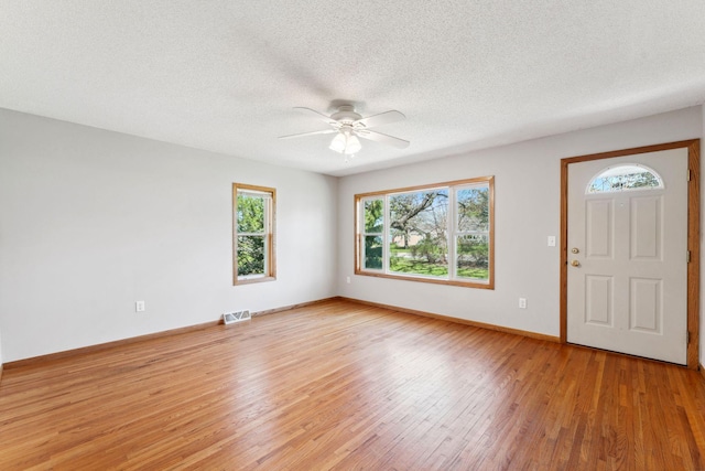 foyer entrance with plenty of natural light, light wood finished floors, ceiling fan, a textured ceiling, and baseboards