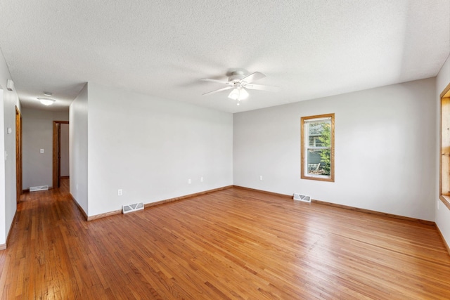 empty room featuring a ceiling fan, light wood finished floors, baseboards, and a textured ceiling