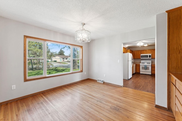 unfurnished dining area featuring wood finished floors, a chandelier, baseboards, and a textured ceiling