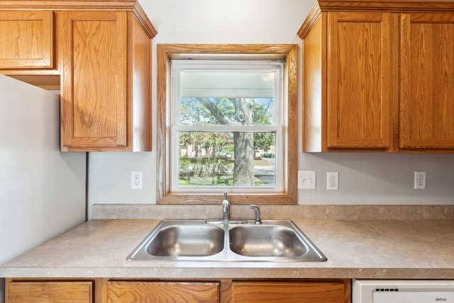 kitchen featuring a sink, dishwasher, light countertops, and brown cabinetry