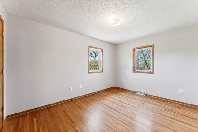 empty room featuring light wood-type flooring, baseboards, and a textured ceiling
