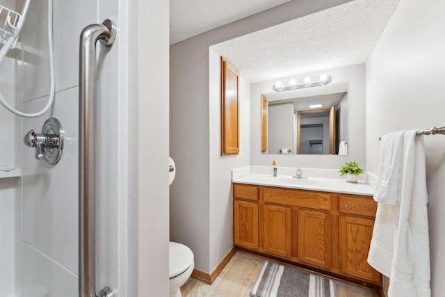 bathroom with a shower stall, toilet, vanity, baseboards, and a textured ceiling