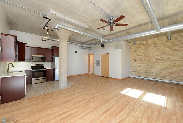 unfurnished living room featuring a sink, ceiling fan, brick wall, light wood finished floors, and baseboards