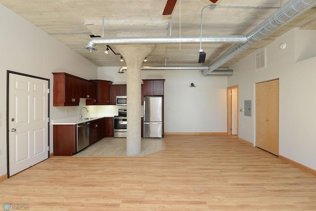 kitchen featuring appliances with stainless steel finishes, a sink, light countertops, light wood finished floors, and a towering ceiling