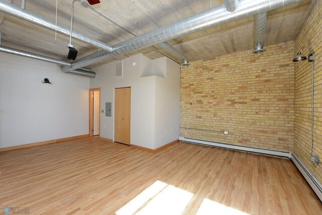 unfurnished room featuring brick wall, wood finished floors, baseboards, and a baseboard heating unit