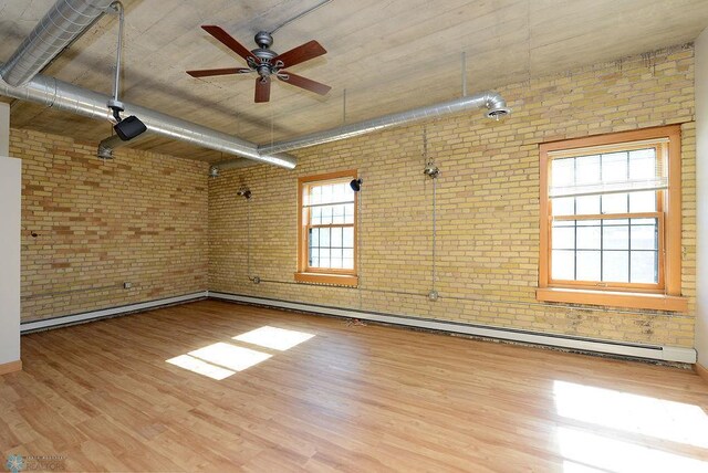 unfurnished room featuring brick wall, a ceiling fan, wood finished floors, and a baseboard heating unit