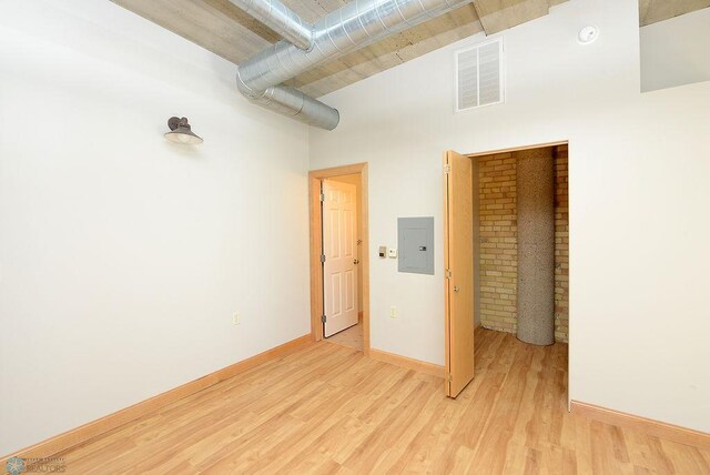 empty room featuring electric panel, light wood-style flooring, baseboards, a smoke detector, and a towering ceiling