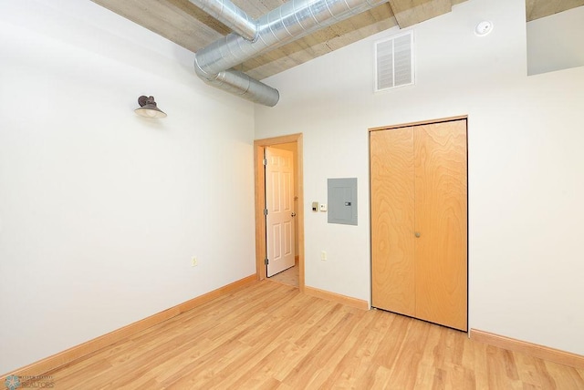 unfurnished bedroom with electric panel, light wood-style flooring, baseboards, and a high ceiling