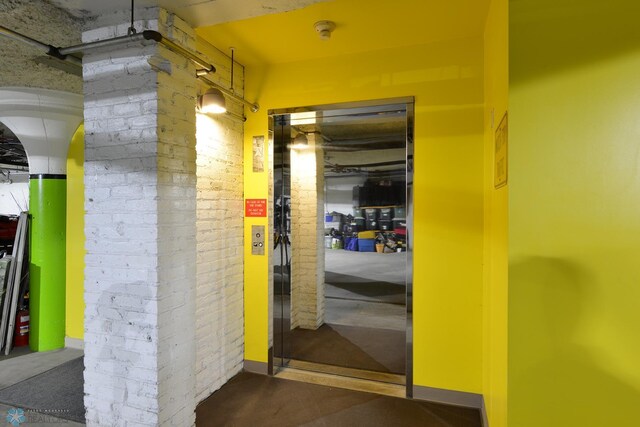 corridor featuring concrete flooring, brick wall, and elevator
