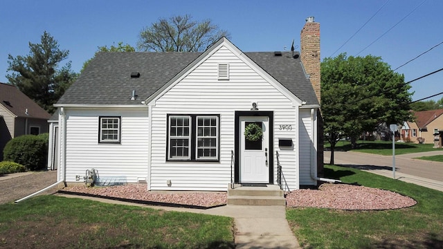 view of front of home with a chimney, a front yard, and a shingled roof