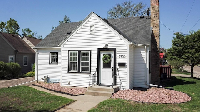view of front facade with a chimney, a front lawn, and a shingled roof