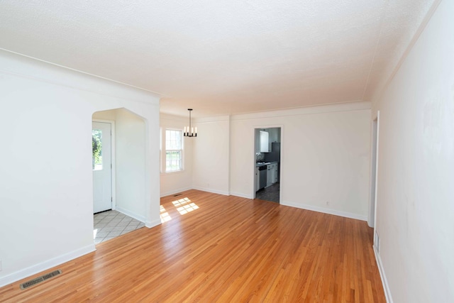 empty room featuring a chandelier, light wood-style floors, arched walkways, and baseboards