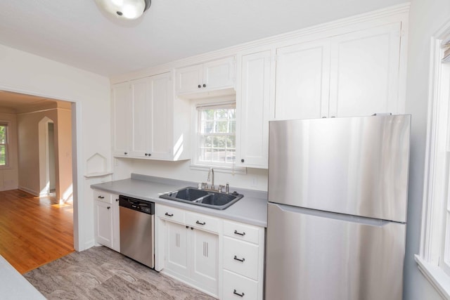 kitchen with stainless steel appliances, a sink, white cabinetry, light countertops, and arched walkways