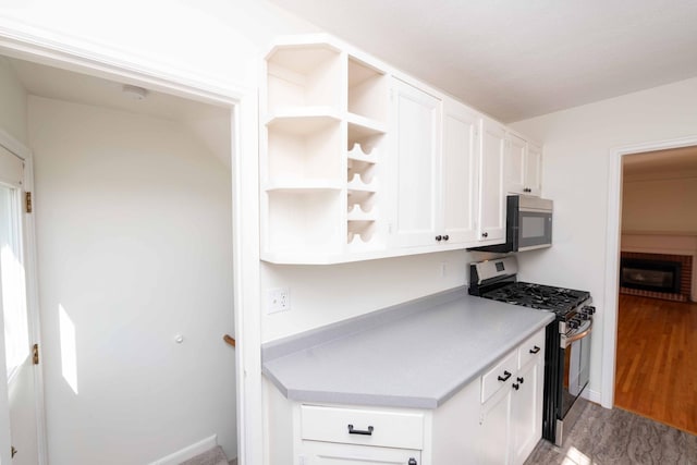 kitchen with appliances with stainless steel finishes, white cabinetry, light countertops, open shelves, and wood finished floors