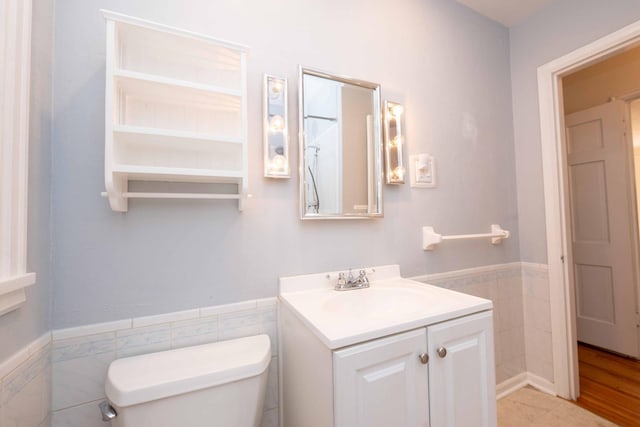 bathroom featuring tile walls, toilet, a wainscoted wall, and vanity