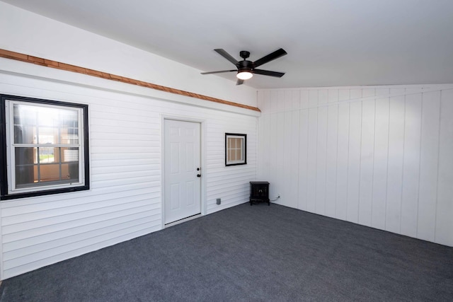 empty room featuring dark carpet, a ceiling fan, and wood walls