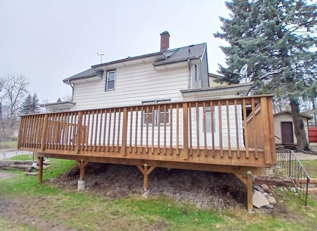 rear view of house with a chimney, a deck, a storage unit, and an outdoor structure