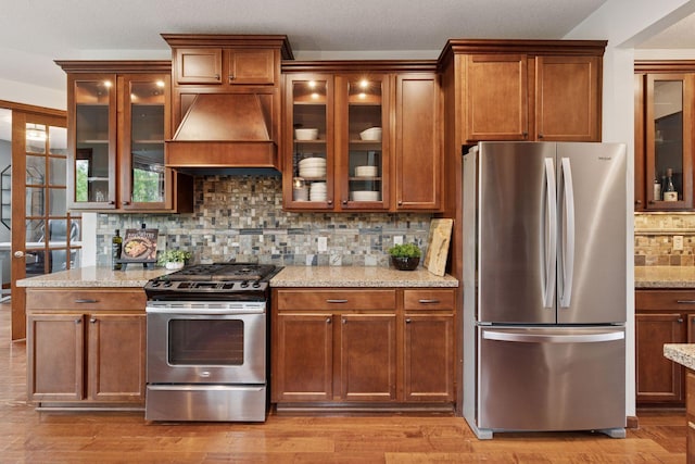 11200 Walnut Ln, Woodbury, MN 55129 - kitchen with stainless steel appliances, custom exhaust hood, decorative backsplash, light stone counters, and glass insert cabinets