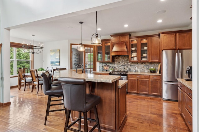 11200 Walnut Ln, Woodbury, MN 55129 - kitchen featuring appliances with stainless steel finishes, brown cabinets, custom exhaust hood, tasteful backsplash, and a breakfast bar area