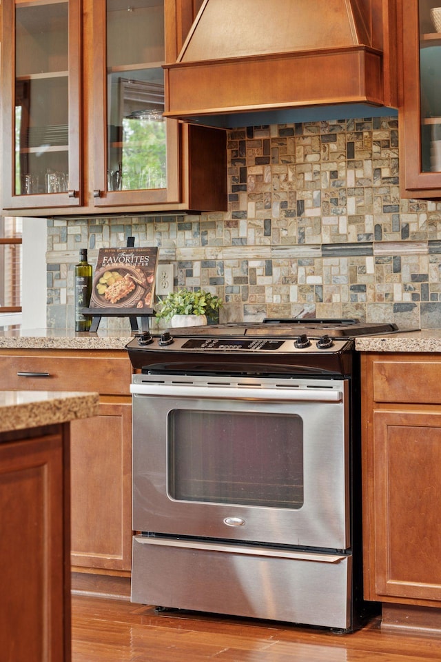 11200 Walnut Ln, Woodbury, MN 55129 - kitchen featuring stainless steel range oven, custom exhaust hood, light wood-style flooring, decorative backsplash, and light stone countertops