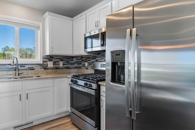 1120 7th Ave NE, Isanti, MN 55040 - kitchen with stainless steel appliances, white cabinets, light stone counters, tasteful backsplash, and light wood-style flooring