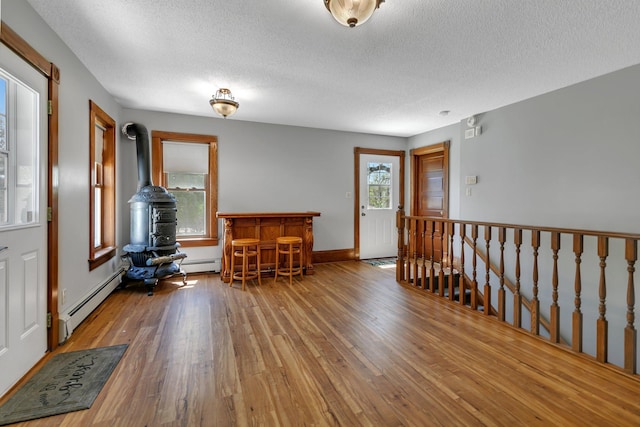 living area with wood finished floors, an upstairs landing, a baseboard heating unit, a textured ceiling, and a dry bar