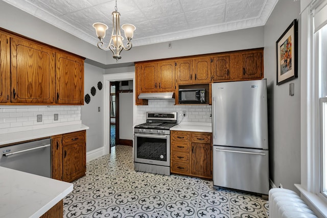 kitchen featuring appliances with stainless steel finishes, under cabinet range hood, light countertops, decorative backsplash, and an ornate ceiling