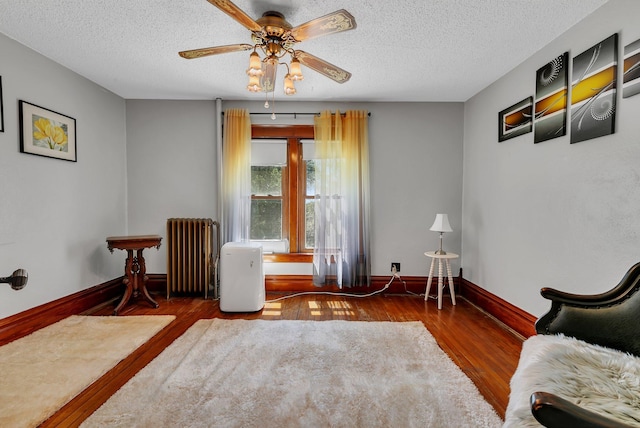 sitting room featuring radiator heating unit, wood finished floors, a ceiling fan, a textured ceiling, and baseboards