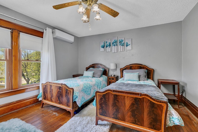 bedroom featuring a wall mounted air conditioner, hardwood / wood-style flooring, baseboards, ceiling fan, and a textured ceiling