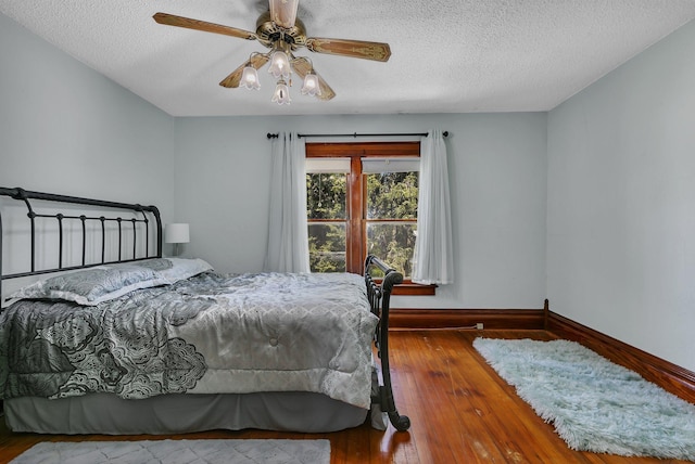 bedroom with a textured ceiling, wood-type flooring, baseboards, and a ceiling fan