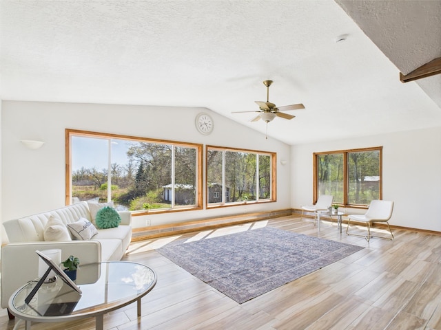 living area with lofted ceiling, a textured ceiling, ceiling fan, light wood-style floors, and baseboards