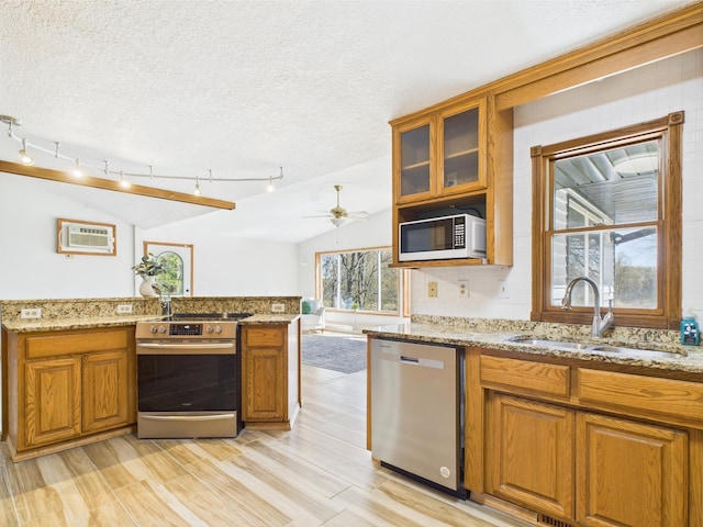 kitchen with stainless steel appliances, a sink, brown cabinets, a wall mounted AC, and lofted ceiling