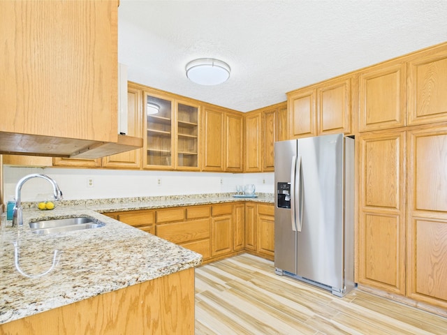 kitchen with stainless steel fridge, a sink, light stone countertops, light wood-style floors, and glass insert cabinets