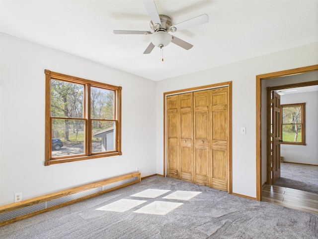 unfurnished bedroom with baseboard heating, multiple windows, carpet flooring, and baseboards