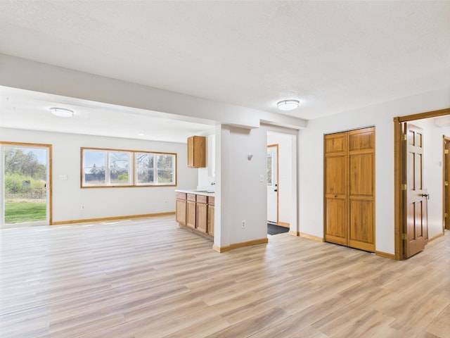 unfurnished living room with light wood finished floors, baseboards, and a textured ceiling