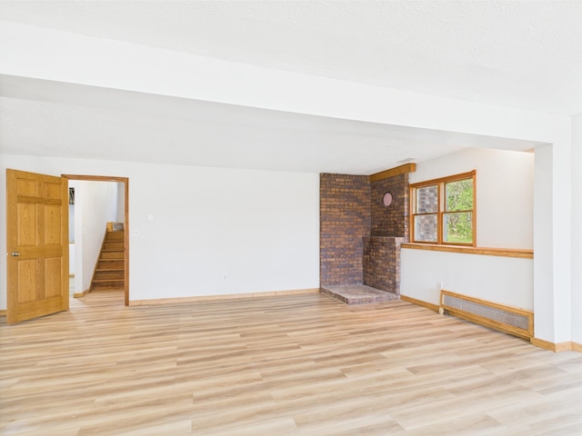 unfurnished living room with radiator heating unit, light wood finished floors, baseboards, and a fireplace