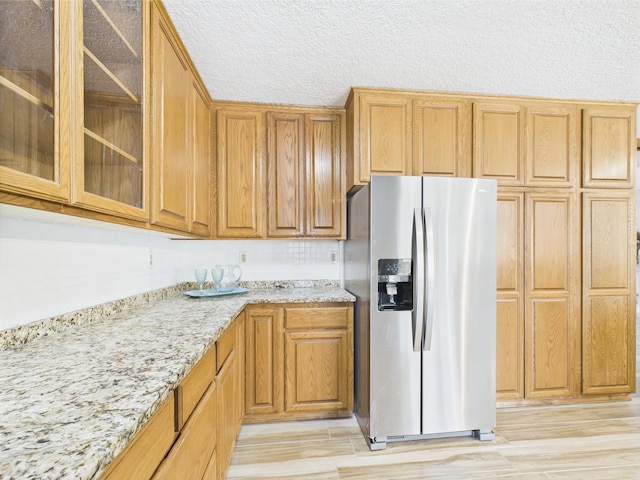 30145 Fir Trl, Stacy, MN 55079 - kitchen with stainless steel fridge, light stone counters, glass insert cabinets, light wood-style flooring, and brown cabinets