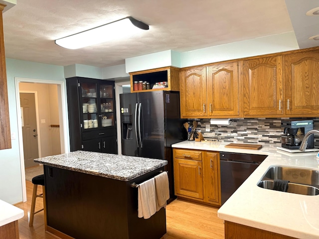 kitchen with black dishwasher, a sink, light wood-style floors, a center island, and backsplash